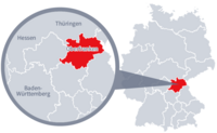 Diese Grafik zeigt eine Karte von Deutschland mit einer detaillierten Ansicht der Region Oberfranken. Oberfranken ist in Rot hervorgehoben und liegt im südlichen Teil Deutschlands. Ein Lupensymbol vergrößert diesen Bereich, um die Lage genauer darzustellen. 