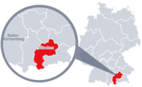 Diese Grafik zeigt eine Karte von Deutschland mit einer detaillierten Ansicht der Region München. München ist in Rot hervorgehoben und liegt im südlichen Teil Deutschlands. Ein Lupensymbol vergrößert diesen Bereich, um die Lage genauer darzustellen. 